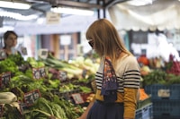 woman standing in front of vegetables in market during day time