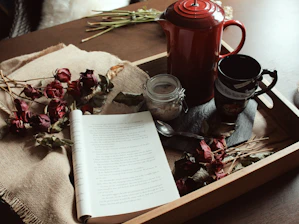 opened book near spoon, flowers, mug and pitcher on tray