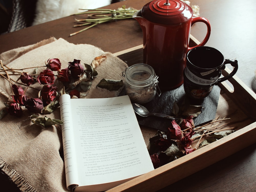 livro aberto perto de colher, flores, caneca e jarro na bandeja