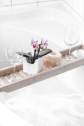 Bamboo bathtub tray holding a book and a candle beside a filled tub.