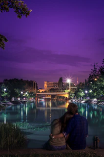 A couple sharing a quiet candlelit dinner beside a gently flowing river under a starlit sky.