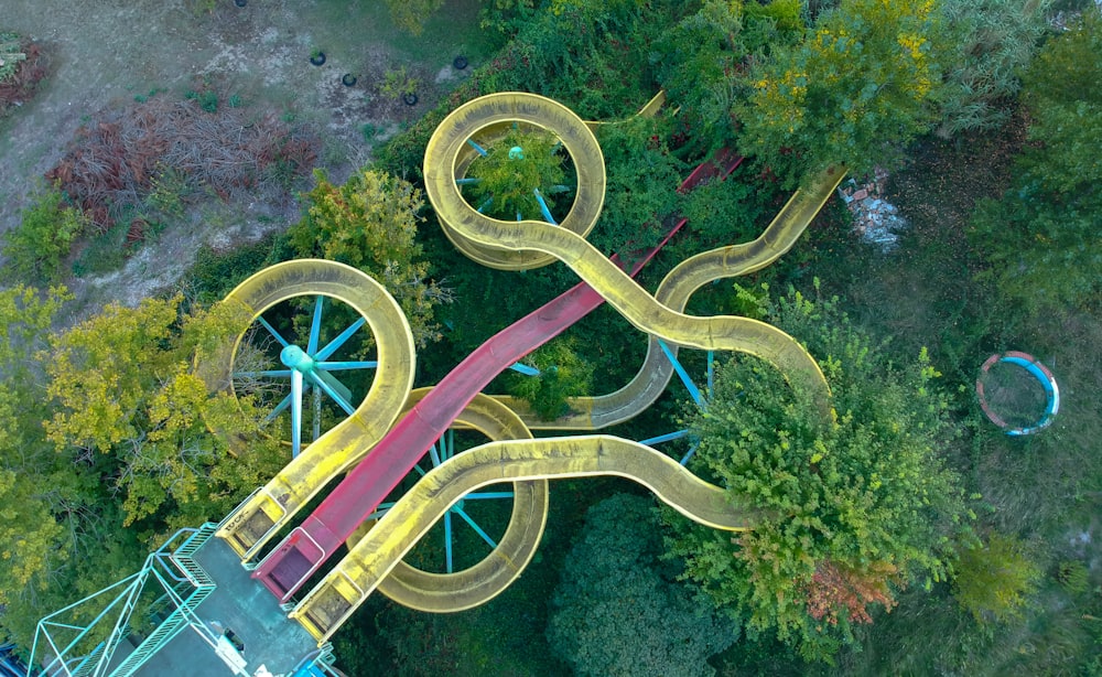 yellow and red metal slides surrounded by green trees at daytime
