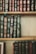 A collection of classic hardcover books with intricate gold designs and lettering on their spines. The books are tightly arranged on wooden shelves, showcasing a variety of titles and authors. The spines are predominantly green, blue, and burgundy, with ornate decorative patterns.