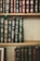 A collection of classic hardcover books with intricate gold designs and lettering on their spines. The books are tightly arranged on wooden shelves, showcasing a variety of titles and authors. The spines are predominantly green, blue, and burgundy, with ornate decorative patterns.