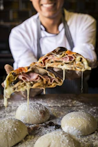 Friendly pizzaiolo tossing pizza dough in the air with a smile.