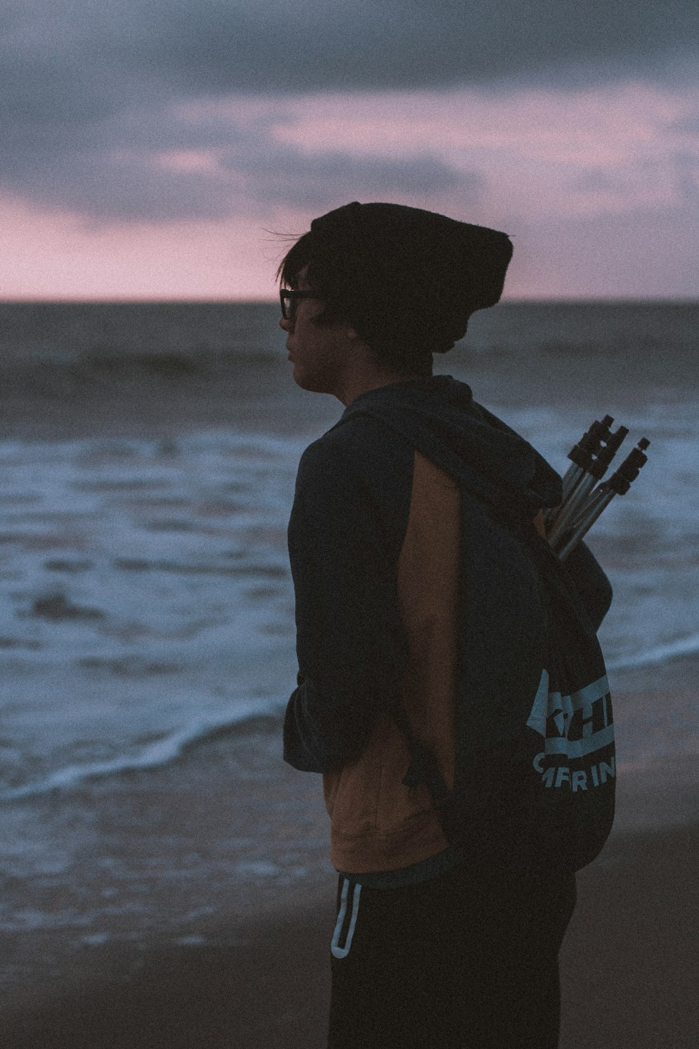 man in black and orange jacket with backpack on seashore