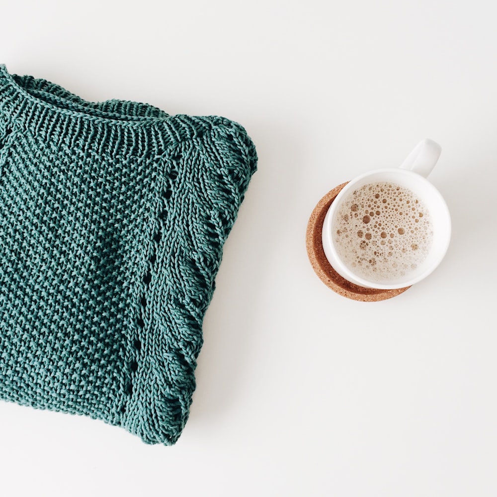 white ceramic mug near the green ribbed shirt