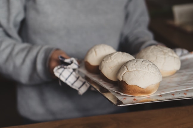 Smiling chef holding a tray of freshly baked bread in a warm kitchen.