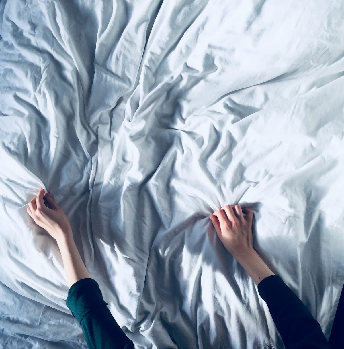 Hands smoothing a crisp white fitted sheet on a bed in soft morning light