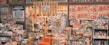 A cluttered storefront of a Japanese retail shop filled with various products, including snacks, groceries, and household items. Brightly colored sale signs in Japanese advertise discounts and promotions, creating a busy and vibrant atmosphere. The shelves and baskets are packed, and the overall space has a crowded appearance.