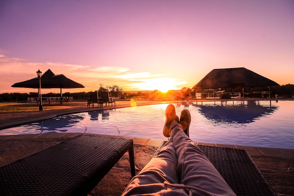 person lying on lounge chair facing at the swimming pool