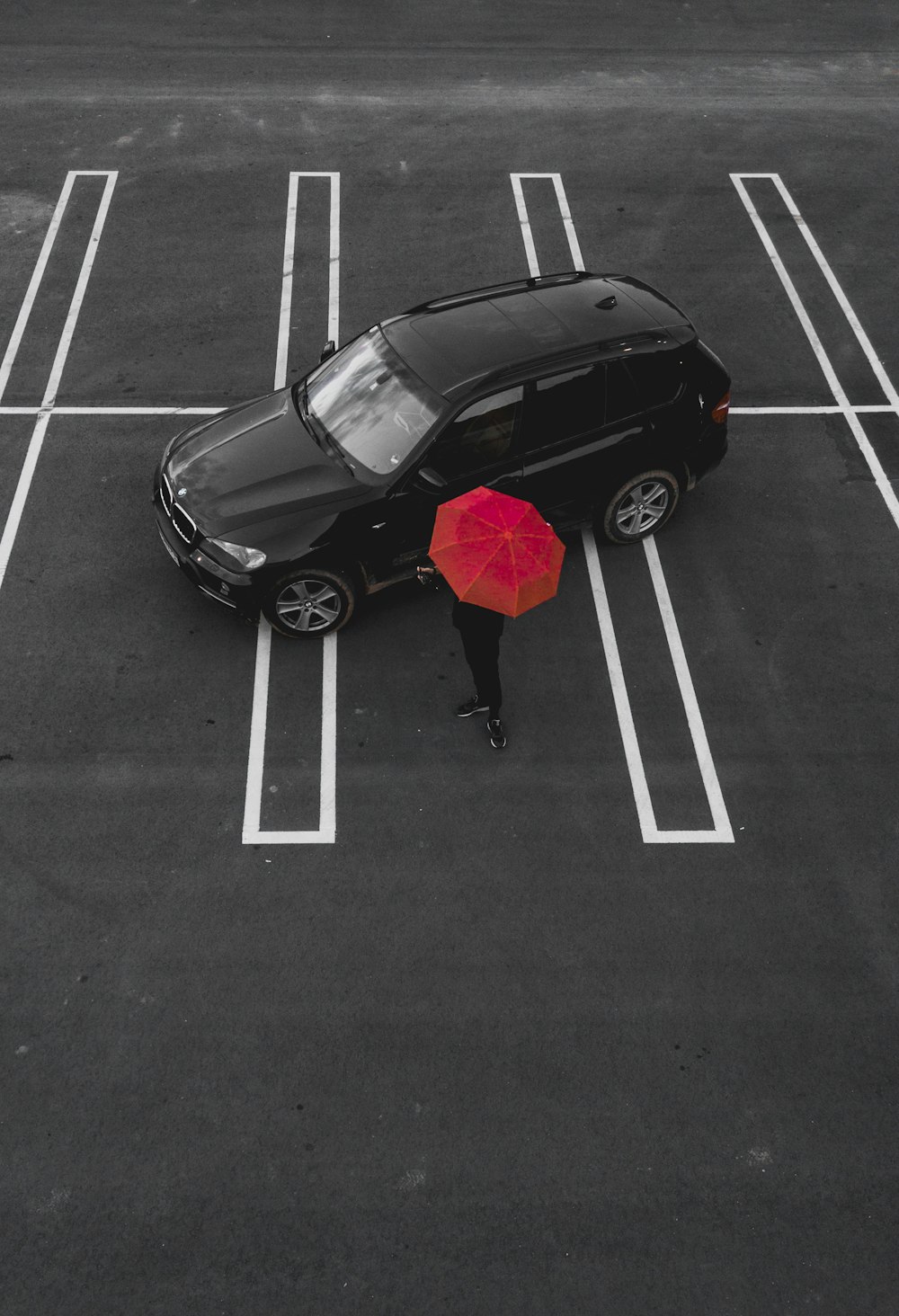 Person mit rotem Regenschirm steht in der Nähe von schwarzem SUV