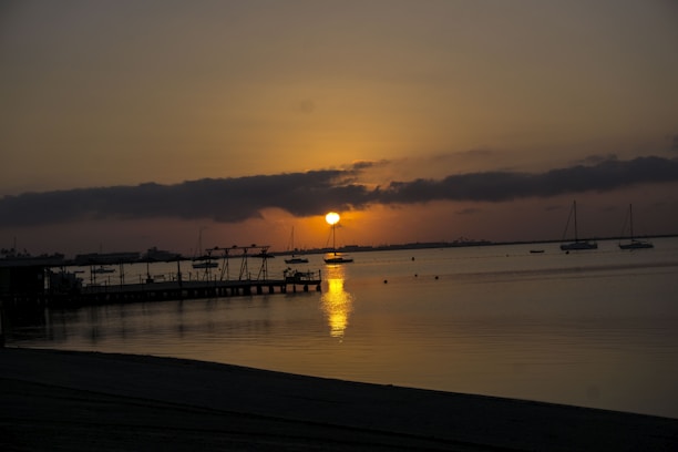 A serene view of sailboats docked at Bear Lake Yacht Club with mountains in the background during sunset.