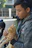 A volunteer gently holding a rescued cat outdoors with a village and mountain slope behind.