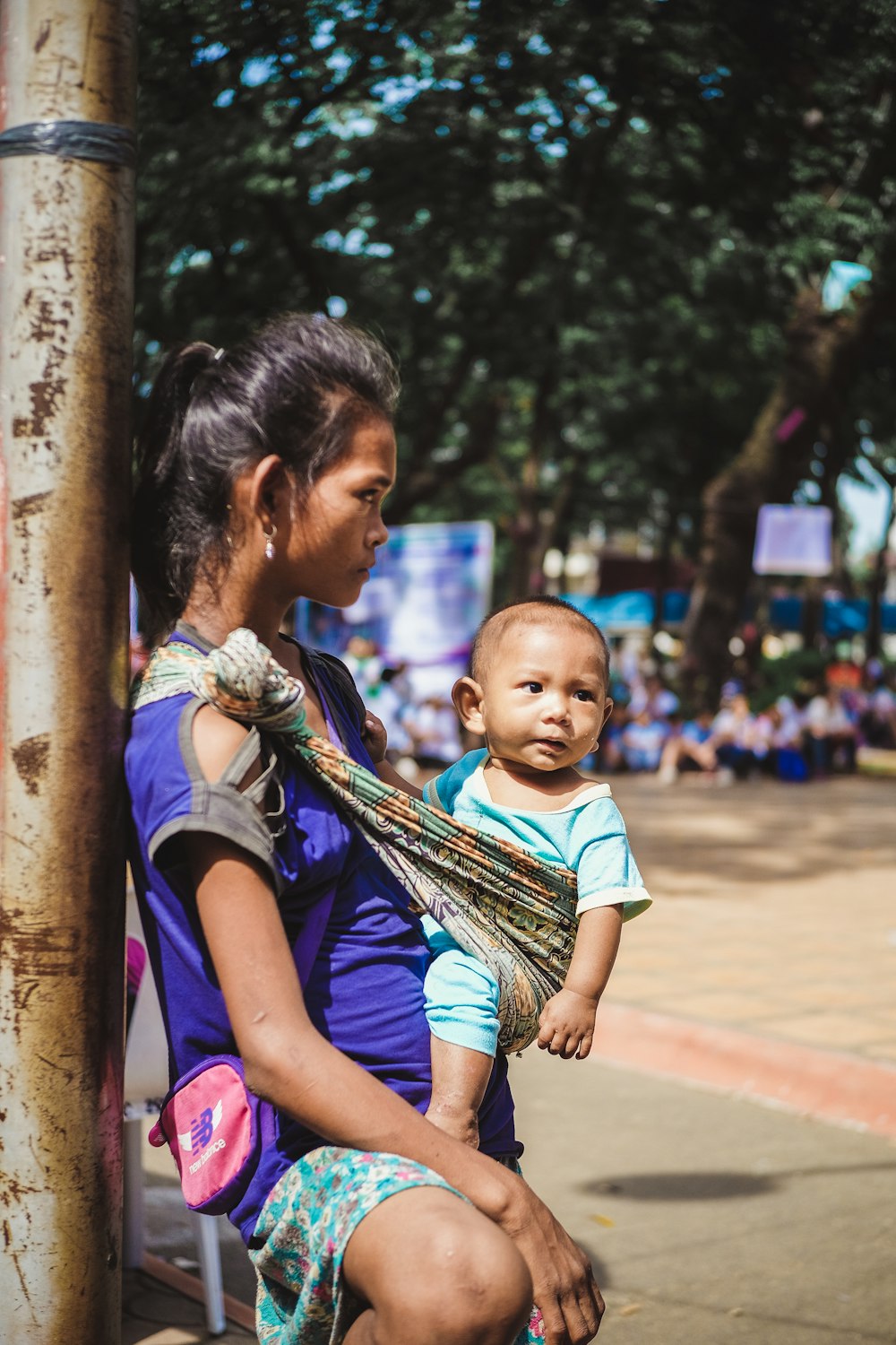 woman carrying her baby while leaning against the brown wooden post