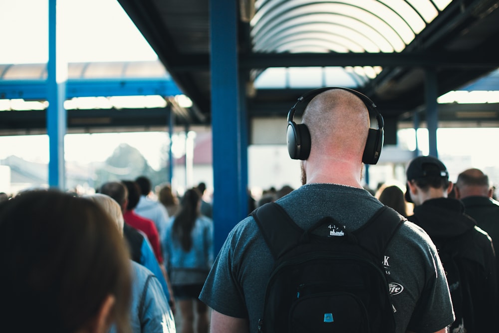 walking man wearing black wireless headphones near people