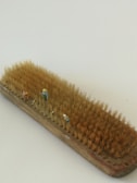 A wooden brush with natural bristles, staged as a miniature scene where small figurines resembling farmers are placed among the bristles, simulating a field with people working.