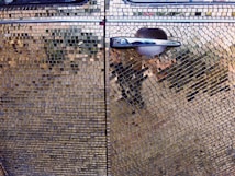 A close-up shot of a car door covered entirely in small, reflective tiles that resemble a mosaic. The car door handle is prominent and has a silver, metallic finish. The tiles create a shimmering effect, displaying various reflections and colors.