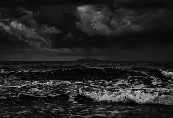 A moody seascape painting showing crashing waves under a cloudy sky.