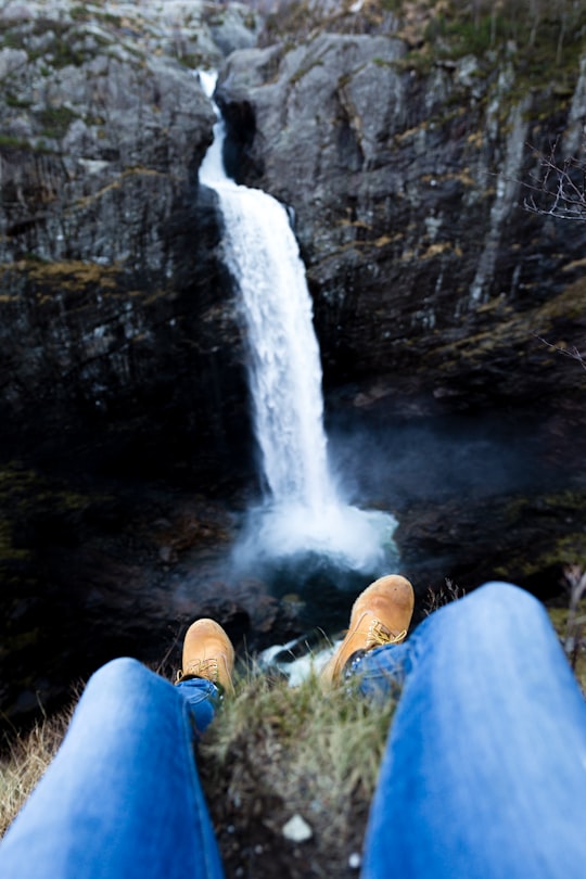 person sitting on cliff near water falls in Frafjordheiane Norway