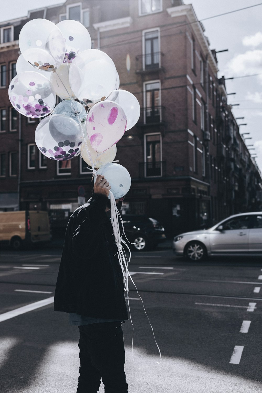 man holding white balloon walking on street during day time