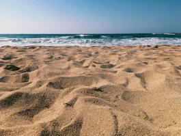 Golden sandy beach just a short walk from the hotel, with gentle waves under a clear blue sky.