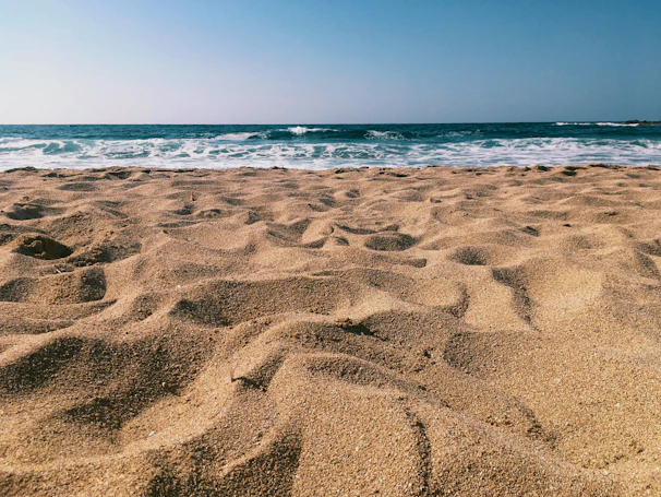 Wide-angle shot of the pristine sandy beach just steps from the guesthouse, waves gently lapping the shore under a clear blue sky