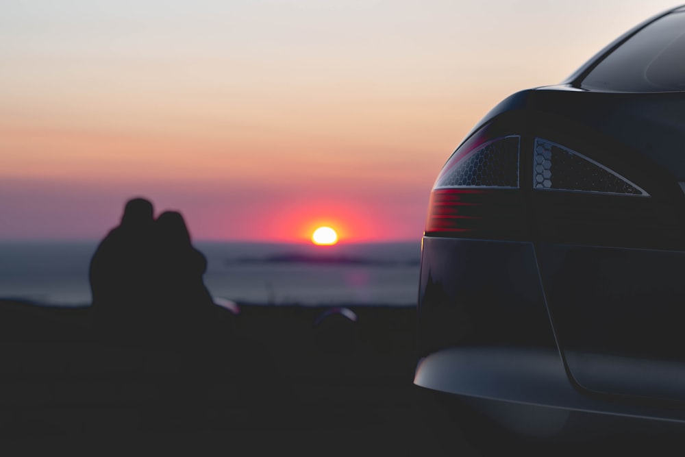 man and woman sitting near body of water watching sunset