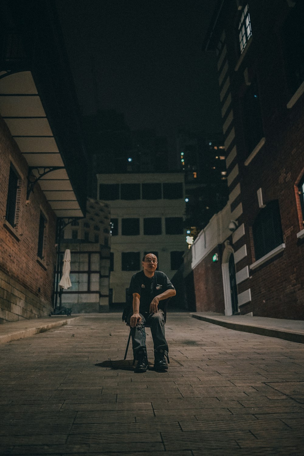 man sitting on chair between brown brick buildings
