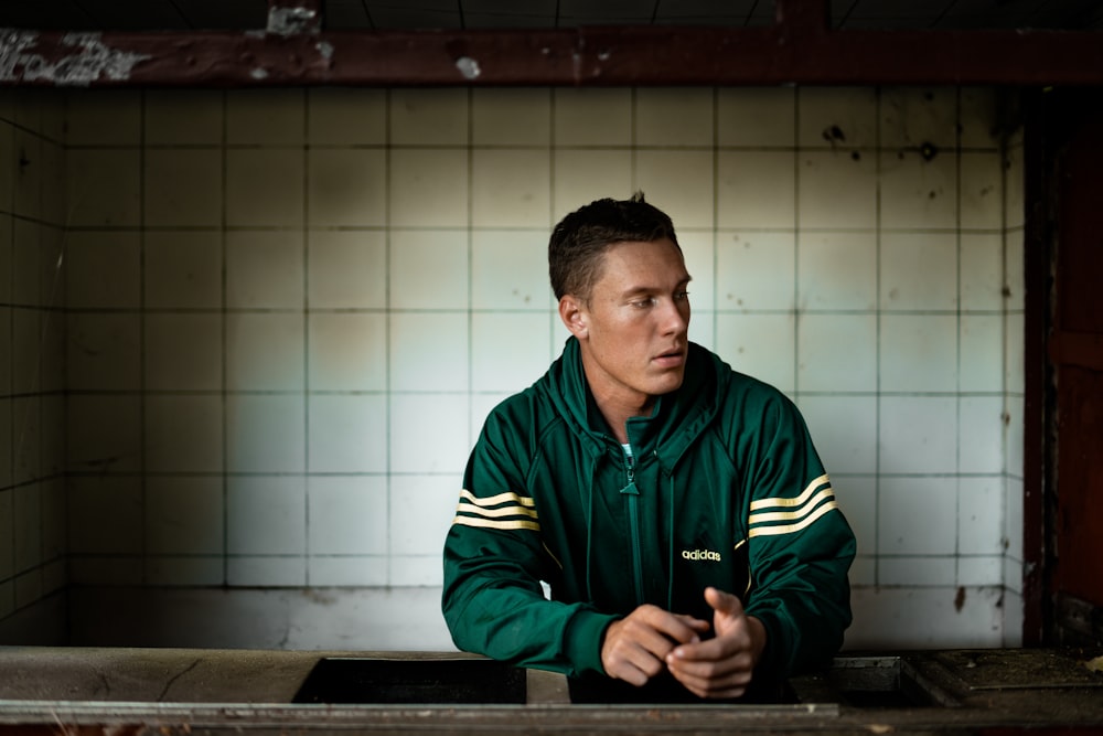 man in green zip-up jacket leaning on countertop