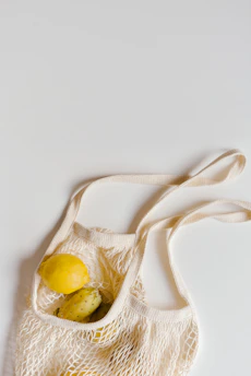 A reusable grocery bag filled with fresh fruits and vegetables on a simple background.