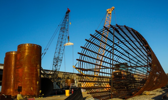 A large industrial construction site with cranes and steel structures under a clear blue sky.