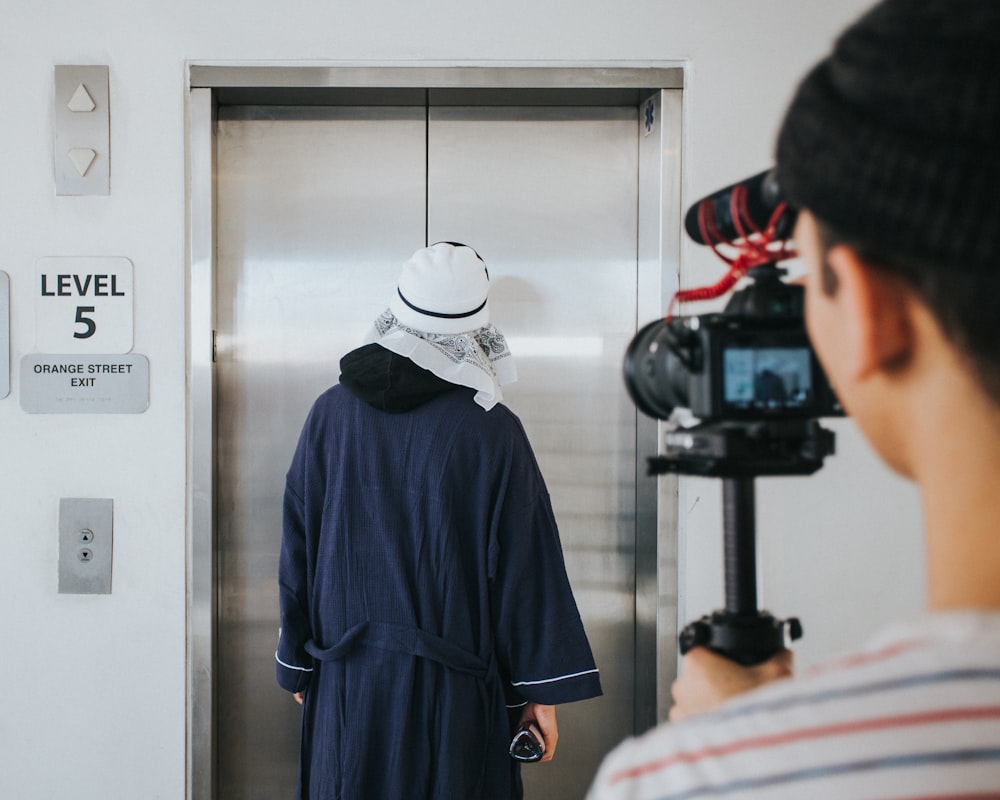 person filming man standing near elevator inside room