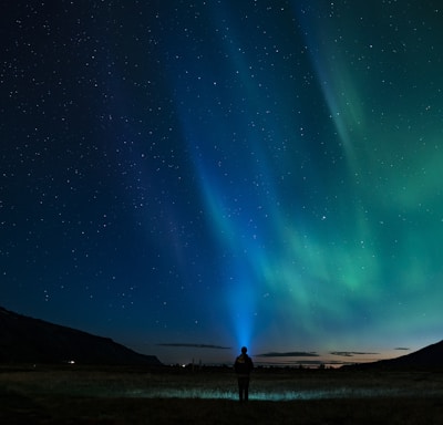 silhouette of person standing under aurora night sky
