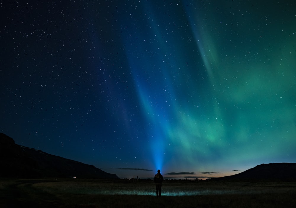 silhouette of person standing under aurora night sky