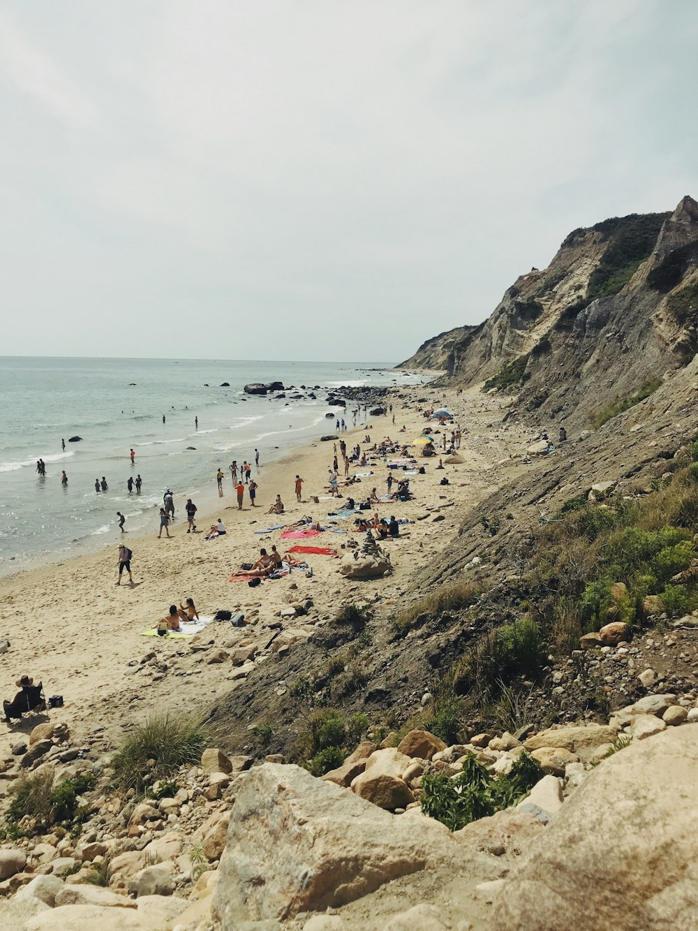 people stand on seashore near gray rock formation