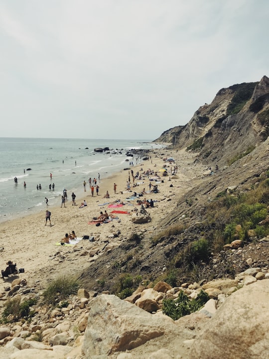 people stand on seashore near gray rock formation in Mohegan Bluffs United States