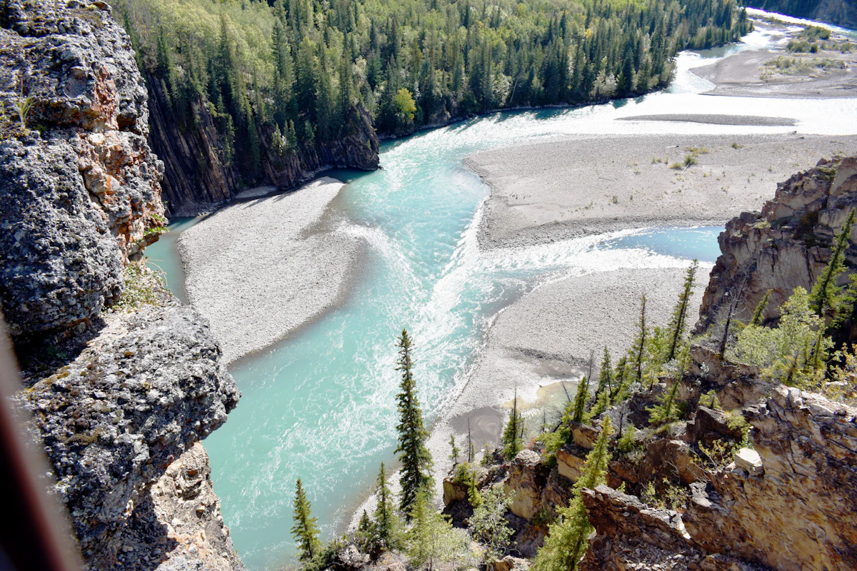 A turquoise river braiding across gravel bars below a rocky cliff near Grande Cache