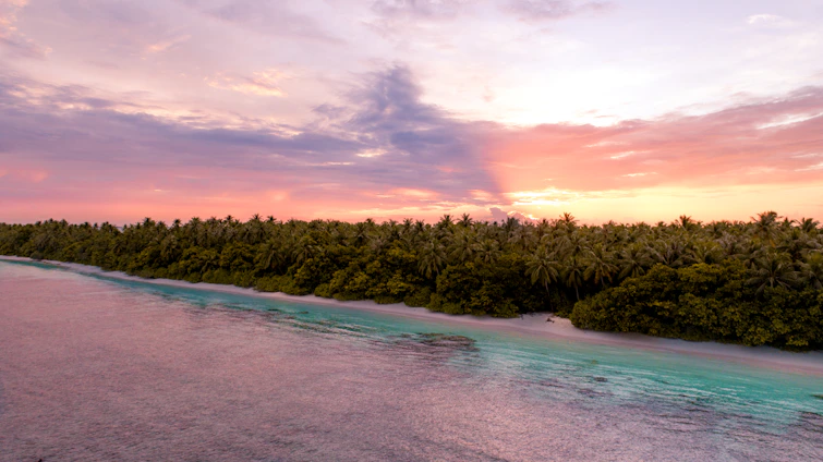 A vibrant photo of an Indonesian beach at sunset with lush green hills in the background.