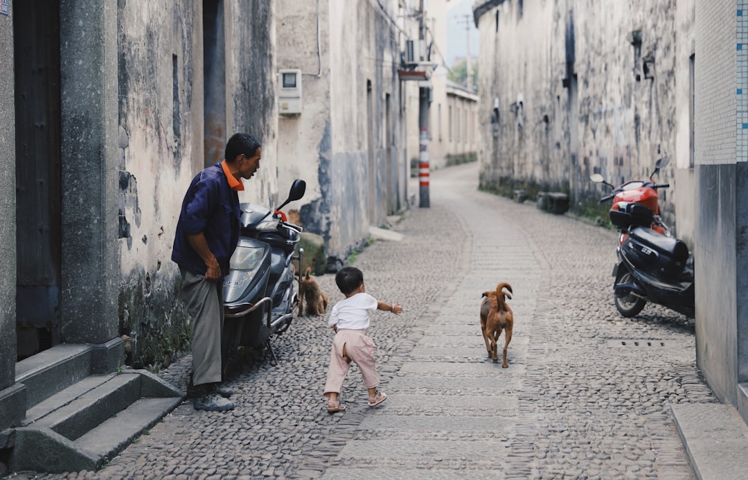 boy walking toward brown dog in between of building at daytime