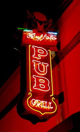 A neon sign with vibrant colors displays the words 'Buffalo Pub and Grill' against a dark background. The sign is predominantly red, with accents of yellow and blue, featuring a stylized image of a buffalo at the top.