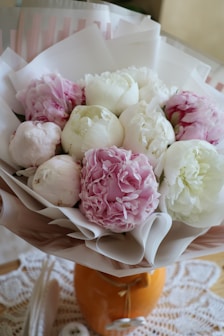 Close-up of a delicate pink peony bouquet resting on a lace-covered table with retro summer decor.