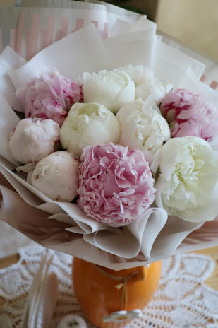 A delicate pastel pink bouquet of roses and peonies arranged elegantly on a white marble table.