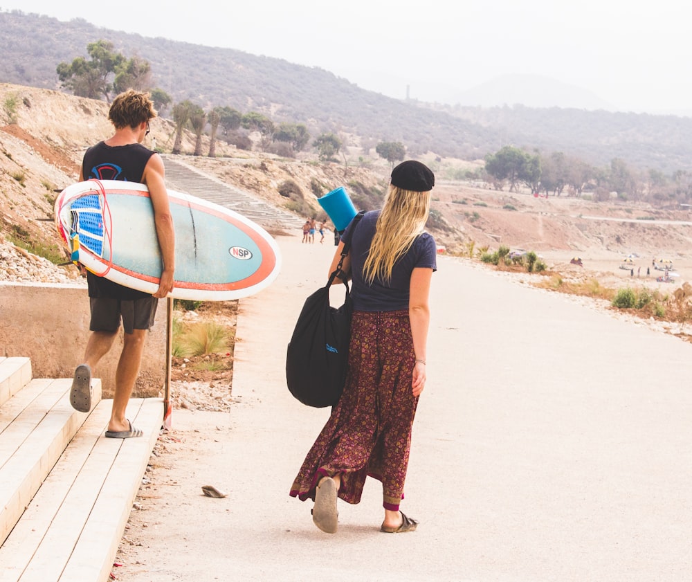 hombre sosteniendo una tabla de surf mientras camina con una mujer