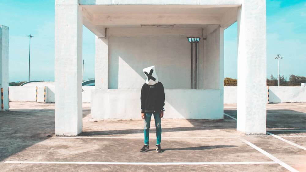 person wearing black sweater and blue pants standing near white wall