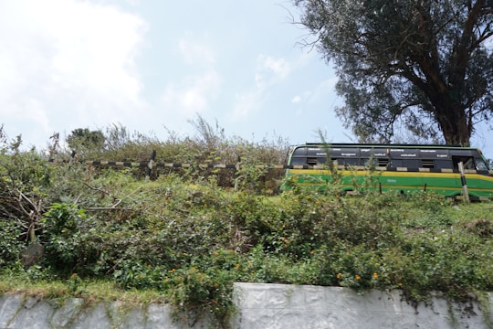 A medium-sized bus with students boarding, set against a backdrop of green hills.