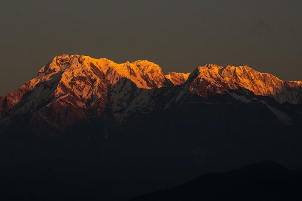 A majestic mountain range with snow-capped peaks glowing in the early morning light.