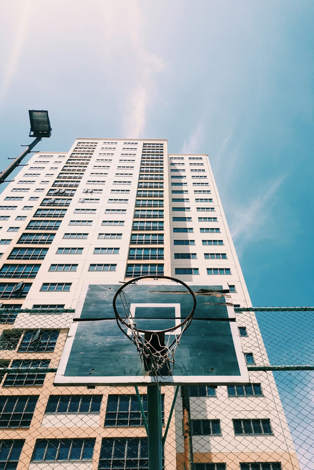 low angle-photography of black and white basketball hoop behind high-rise building during daytime