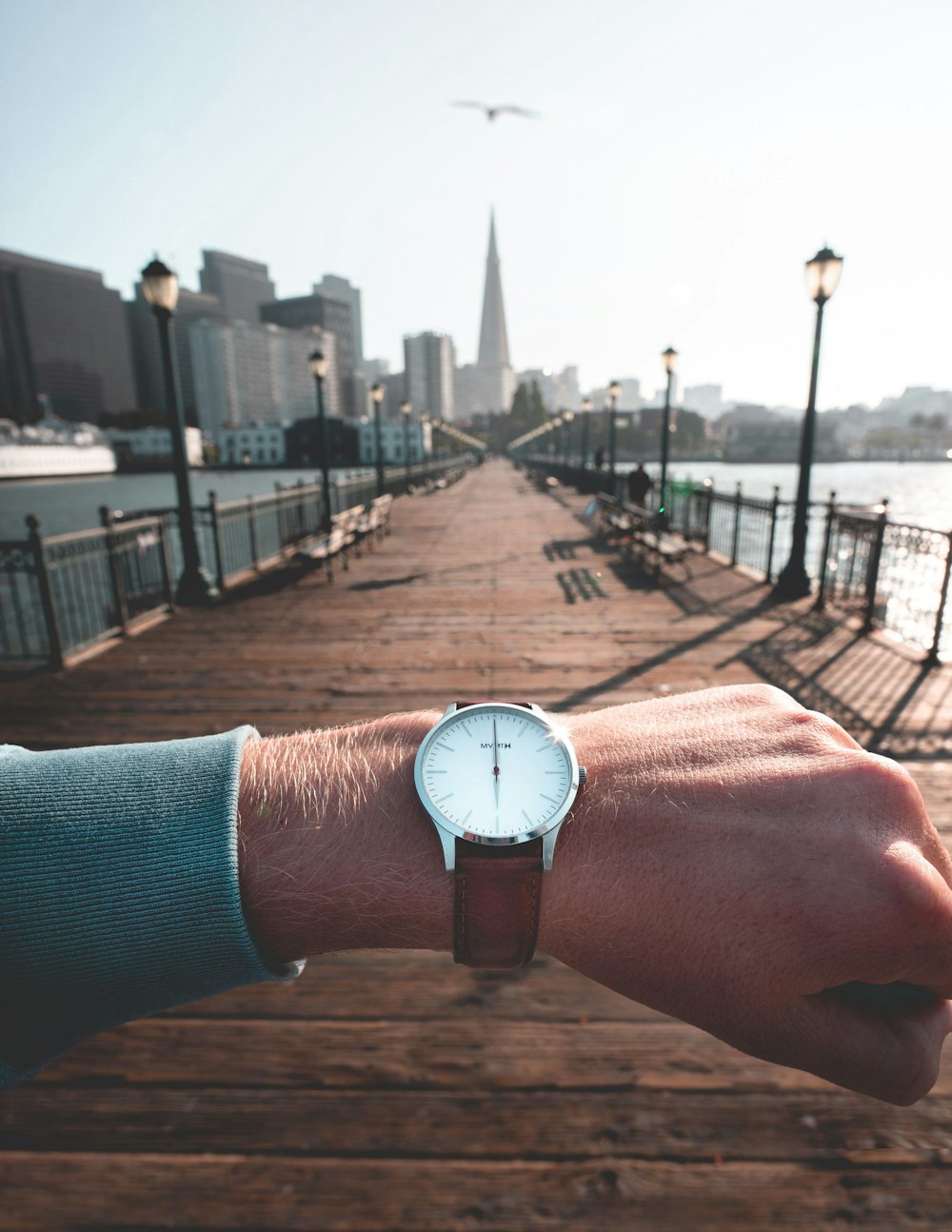 person wearing round silver-colored analog watch with leather band displaying 12:00 time