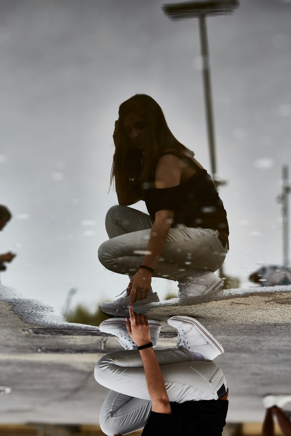 Frau im schwarzen Off-Shoulder-Shirt mit grauer Denim-Jeans, die tagsüber mit ihrem Spiegelbild auf das Wasser zeigt